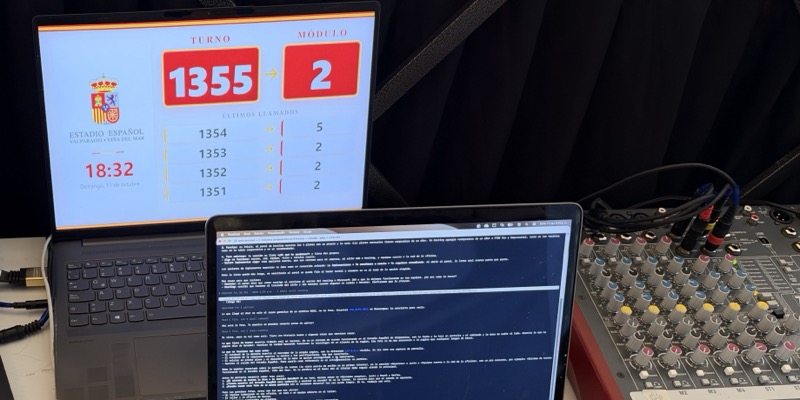 Mesa de control con notebooks, consola de audio y la pantalla del evento.