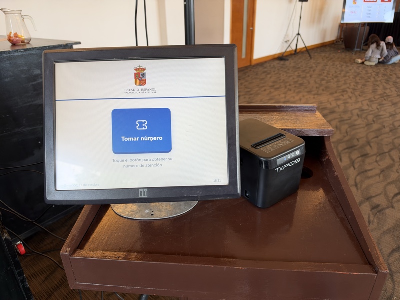 Pantalla táctil con impresora de tickets instalada sobre un mueble de madera.